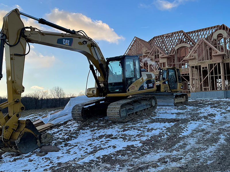 Excavator and bulldozer in front of a framed house
