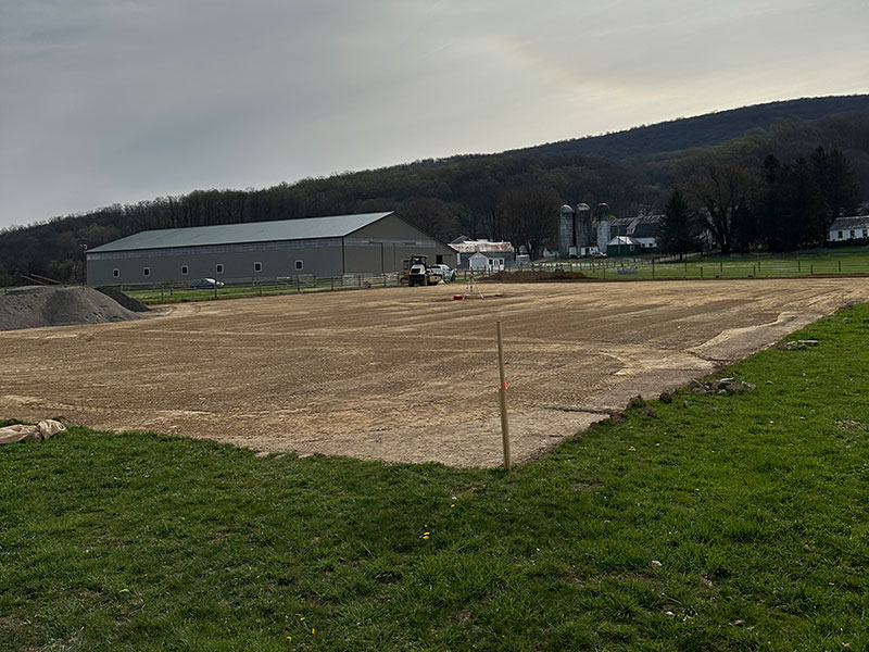 Flat dirt arena with barn in the background